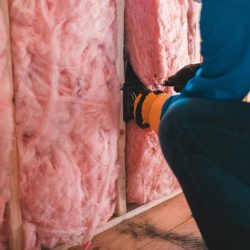 Focused worker installing pink fiberglass insulation in a building interior.