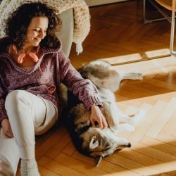 Woman petting her dog while sitting on a wooden floor at home, enjoying a peaceful moment indoors.