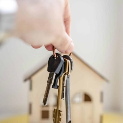 pexels-photo-7599735-7599735 Close-up of a hand holding keys with a miniature wooden house in the background, symbolizing real estate investment.